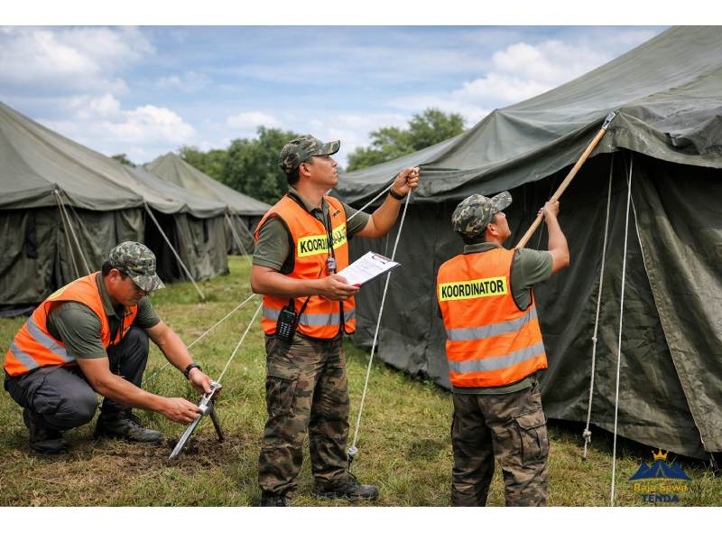 Koordinator lapangan melakukan daily inspection checklist tenda pleton: cek pasak, tali seling, dan atap bebas water pocket